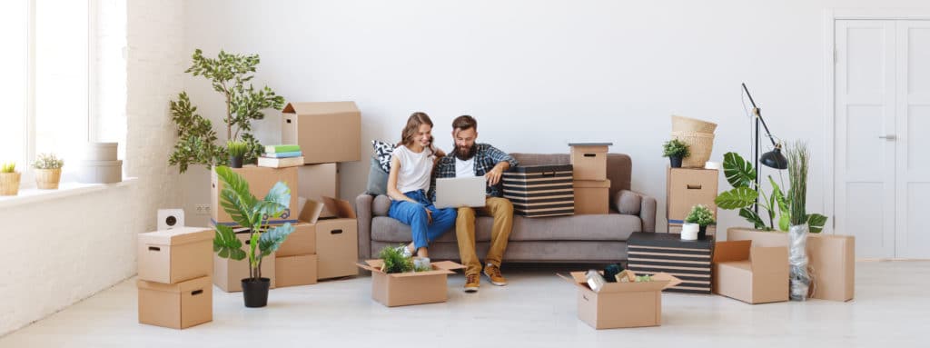happy couple in their new apartment flanked by boxes of their belongings 