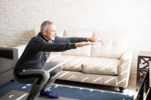 Senior gentleman does squats and bodyweight exercises in his apartment to lose weight