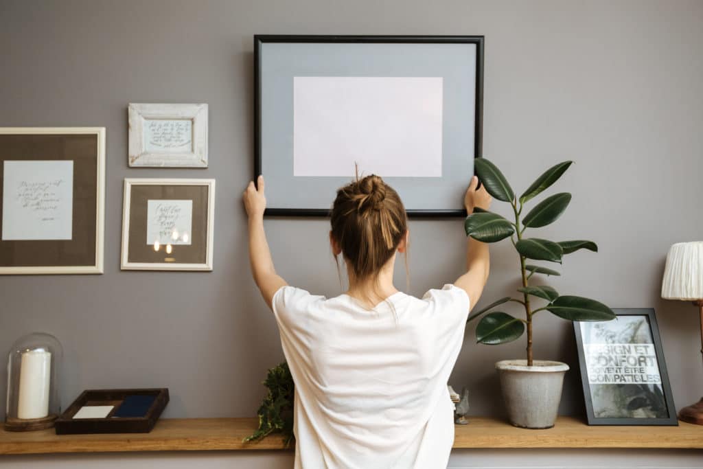 Girl hanging a frame on a gray wall