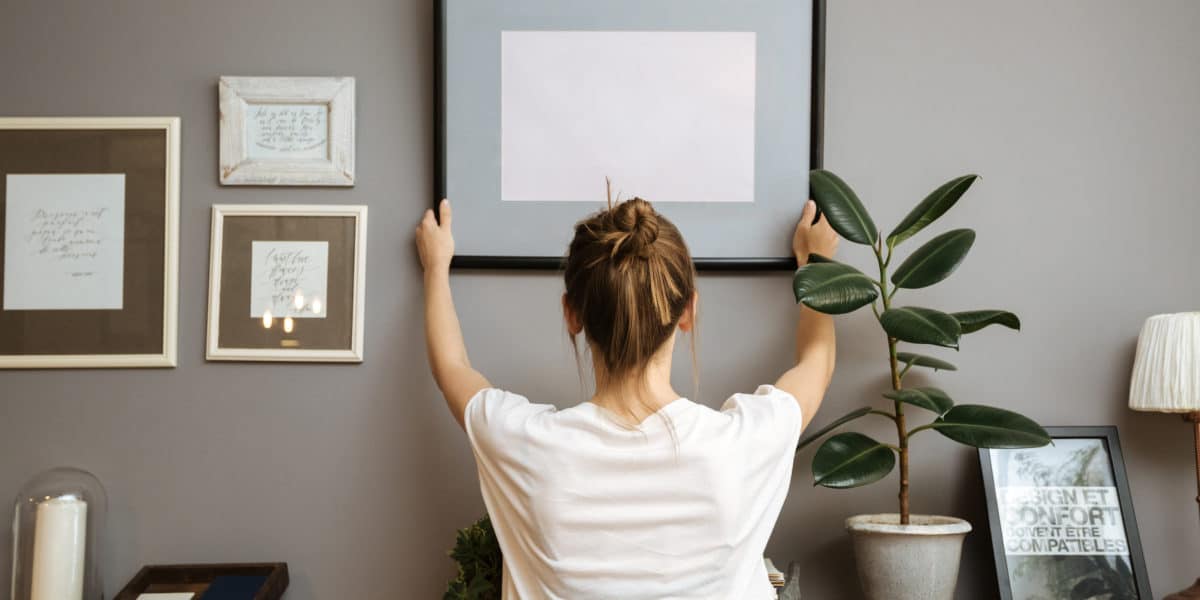 Girl hanging a frame on a gray wall