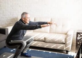 Senior gentleman does squats and bodyweight exercises in his apartment to lose weight